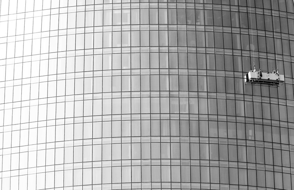 Dramatic shot of window cleaners scaling a glass skyscraper facade.